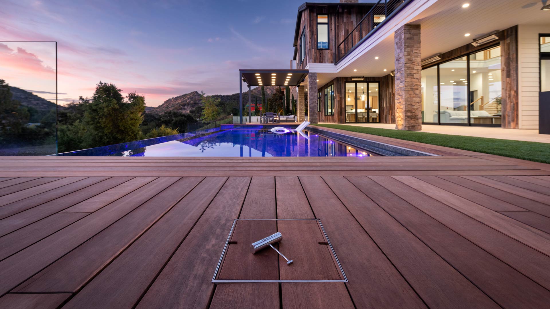 Modern house with a pool at dusk, wooden deck in foreground with a HIDE Skimmer Lid installed into the decking.